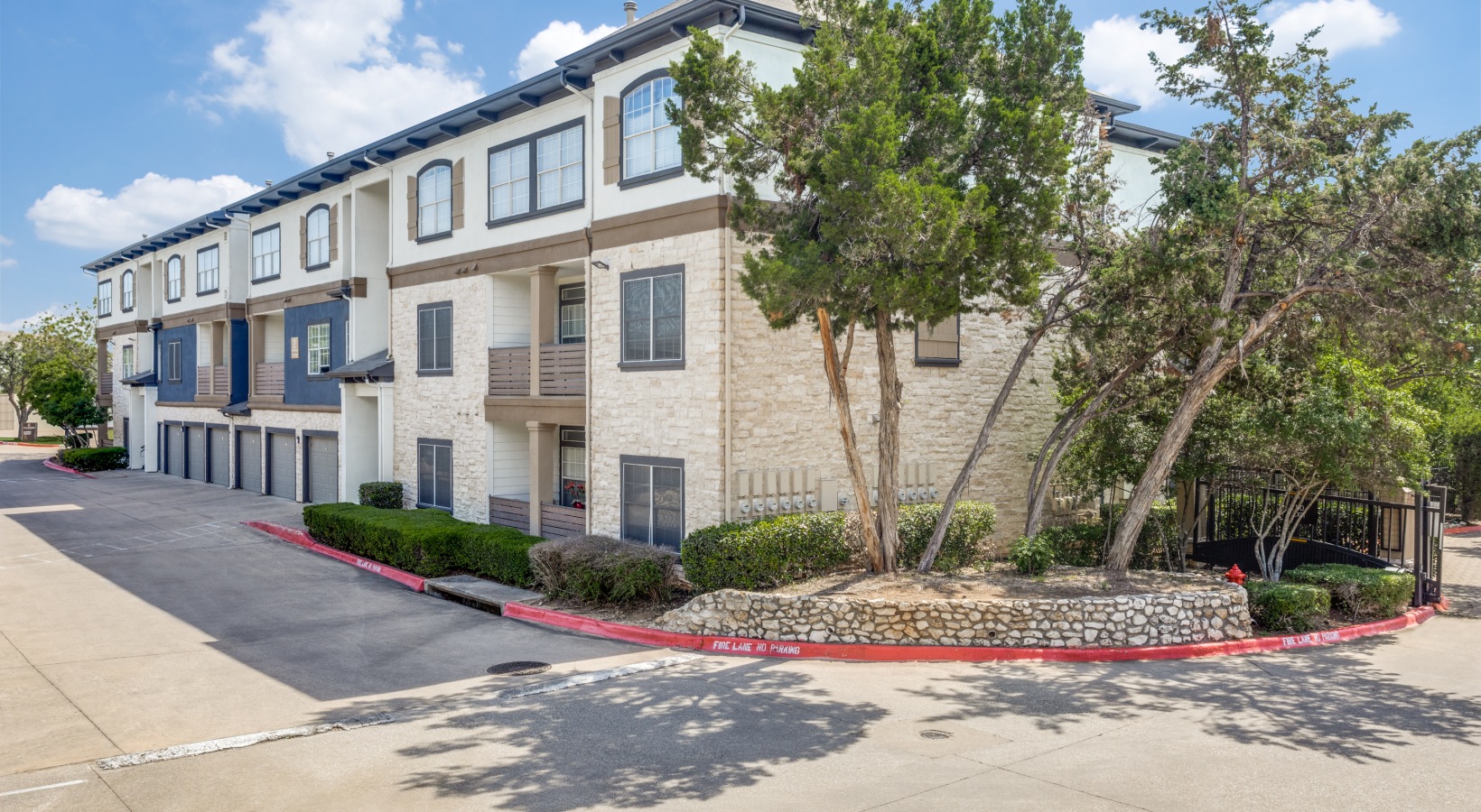 the exterior of an apartment complex with trees and bushes at The Ellwood at Lake Travis